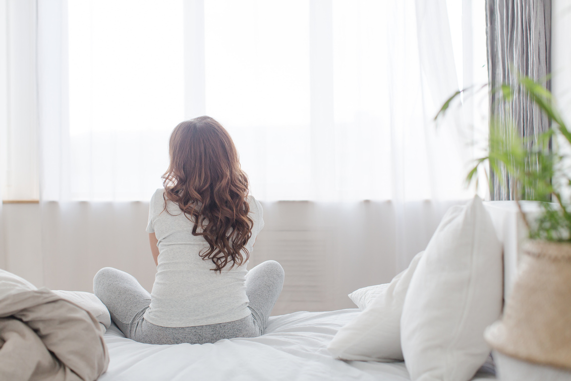Female sitting on bed in morning Back view